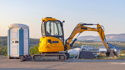 Portable Toilet Cabin and Mini Excavator Machine at Highway Construction Site