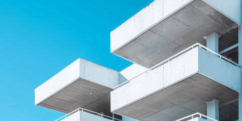 Obraz premium A closeup of white concrete corner apartment building with architectural detail geometric shapes on blue sky background. modern concrete building in blue