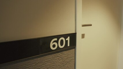 Closeup of hotel room numbers on wall near door. Corridor with lighting in modern tourist hostel. Indication sign 601 numbers of double suite in minimalist style.
