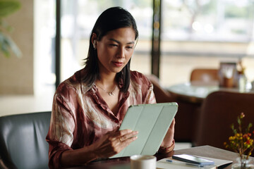 Portrait of businesswoman sitting cafe table and reading article on tablet computer