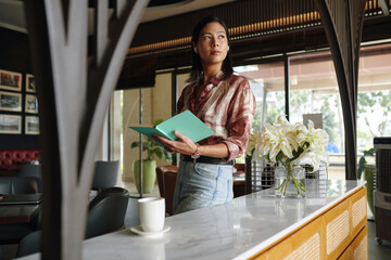Pensive restaurant owner holding planner and looking away