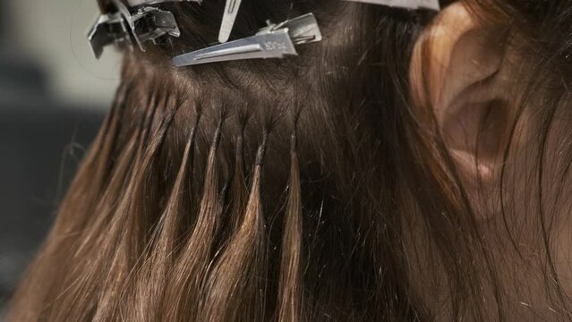 Hair extension with capsules and strands of grown brunette hair in beauty salon, Fusion hair extension with keratin, beauty procedure, increase hair volume. Close up