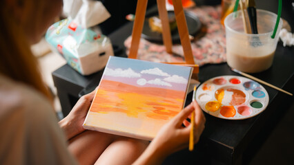 A person is painting with a palette of colors on a table. The table is covered with a floral...