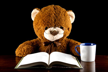 Large Brown Teddy Bear Reading at a Table With Mug of Tea or Coffee - 763967866