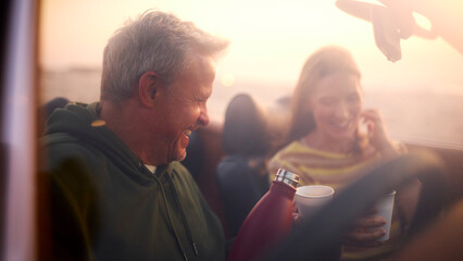 Retired Senior Couple In Classic Sports Car Pouring Hot Drink From Flask At Beach Watching Sunrise