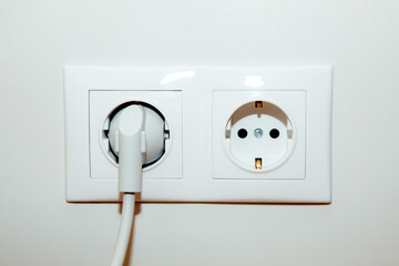 Two white european electrical sockets with an insert plug on a white smooth wall, front view, selective focus