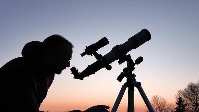 Amateur astronomer looking at the evening skies, observing planets, stars, Moon and other celestial objects with a telescope.