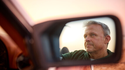 Retired Senior Man Reflected In Mirror Of Classic Open Top Sports Car At Beach Watching Sunrise