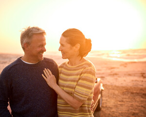 Loving Retired Senior Couple On Vacation Next To Classic Sports Car At Beach Watching Sunrise