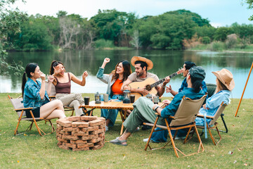 Young friends share a fun summer weekend outdoors with a campfire, bar-b-q, and picnic, celebrating...