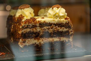 Carrot cake with cream cheese frosting and pecans, a classic dessert, displayed in a bakery window.