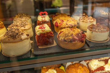 Array of exquisite pastries: frosted cakes, fruit tarts, and cheesecakes temptingly displayed in a bakery window, inviting indulgence.
