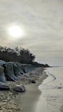 Tranquil parallax seascape of calm Baltic Sea with empty secluded sandy beach and old stone breakwaters at cloudy spring day. With no people vertical panoramic shot rendered in 4K