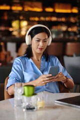 Smiling woman in headphones listening to voice messages on smartphone