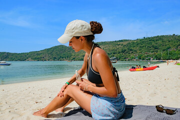 Lebanese young woman applying herself sunscreen on beach and tanning