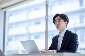 オフィスでパソコンを使って仕事をするスーツを着た若い日本人ビジネスマン