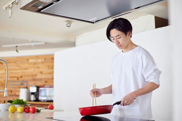 キッチンで料理を作る若い日本人の男性