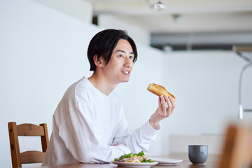 リビングにて朝食を食べる若い日本人の男性