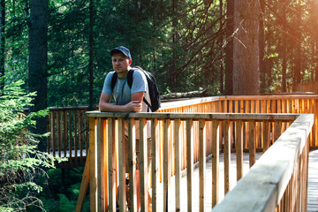 A young man walks through the park. A man with a backpack on his shoulders stands thoughtfully looking at the forest. Spending time outdoors. Front view