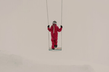 Woman snowboarder dressed in red jumpsuit on swing in the fog in winter mountains