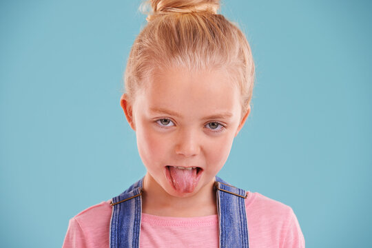Kid, portrait and tongue out in studio for silly, goofy and playful facial expression with blue background. Child, crazy and funny face of young girl for comic gesture, humor and joking for comedy