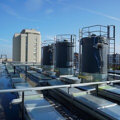 Obraz premium Industrial water tanks paired with solar panels on a city building's rooftop, blending utility with renewable energy solutions
