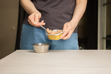 The owner puts wet food in the pet's bowl, feeding the dog, canned food, canine nutrition