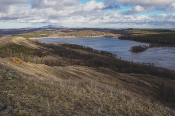 Scenic lake nestled among hills and trees under a vast sky