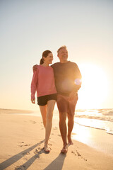 Loving Retired Senior Couple On Vacation Walking Along Beach Shoreline Hugging At Sunrise - 763998677