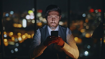 Corporate boss messaging mobile phone at evening city view. Late man work office