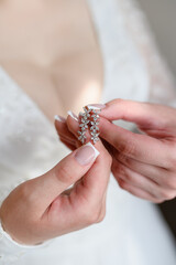 Beautiful earrings in hands of bride, close-up. Concept of bride's morning, preparation for wedding ceremony, wedding day. Stylish wedding accessory for the bride. Vertical.