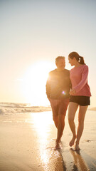 Loving Retired Senior Couple On Vacation Walking Along Beach Shoreline Hugging At Sunrise - 763999039