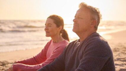 Peaceful Senior Couple Relaxing Sitting On Beach Shoreline With Closed Eyes At Sunrise Together - 763999231
