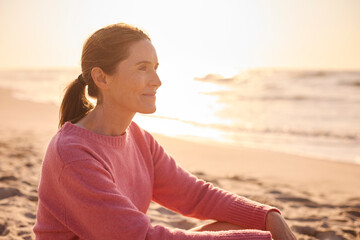 Fototapeta na wymiar Retired Senior Woman On Vacation Sitting On Beach Shoreline Watching Sunrise