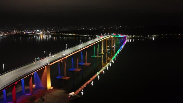 Drone night view of Tasman Bridge with reflection on water lit up in rainbow colors for Pride Week