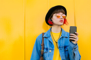 Fashionable Non-Binary Person in Denim In Front of Yellow Wall with Smartphone in Hands