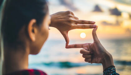 hands frame the sun over blurred ocean at sunset, symbolizing future success and business mindset