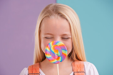 Child, lollipop and candy dessert in studio fr party snack at carnival or rainbow swirl, eating or...