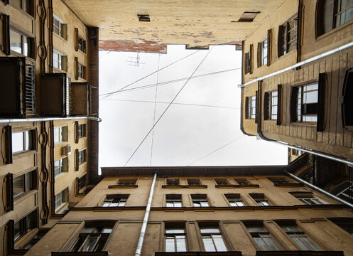 A symmetrical view of a building's courtyard with architectural details, looking up towards. Dark inner courtyard perspective, an old living houses in Saint-Petersburg, Russia
