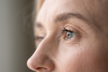 A close-up depicts part of a womans face, highlighting her eye, eyelashes, and the texture of her skin. Her gaze seems reflective and introspective, capturing a moment of thought or observation
