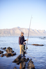 Father, fishing rod and young boy on rocks, teaching and bonding for activity by ocean. Sea, teach and learn to fish for childhood development, winter and hobby together while on countryside vacation