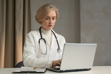 A professional senior female doctor, with a stethoscope around her neck, is intently reviewing data...
