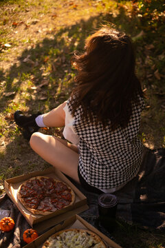 A woman enjoys a spring picnic in the park, savoring pizza on a warm day, depicting outdoor weekend leisure and promoting a pizzeria.