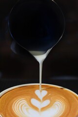 Barista making a cup of coffee latte art with dark background.