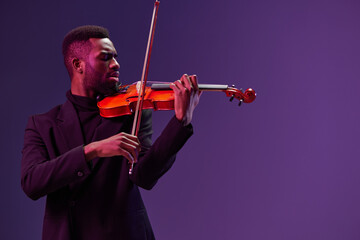 African American musician in black suit playing violin on purple background in elegant performance...