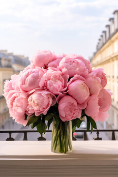 Beautiful pink peonies in a glass vase with view to old town with beautiful architecture.