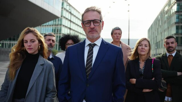 A team of diverse business people in formal suit looking confident and serious at camera gathered outside the work building. The leader steps forward showing himself to be the boss