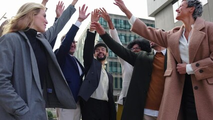 Cheerful group of diverse business people in formal wear are gathered in a circle, sharing smiles and stacking hands together as a gesture of unity and celebration success at a formal event