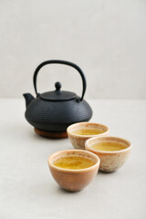 Black cast iron teapot and three ceramic cups of green tea - 764037217