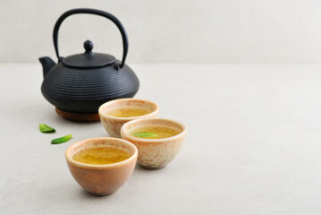 Black cast iron teapot and three ceramic cups of green tea - 764037245